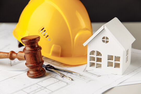 Wooden gavel with yellow helmet and house close-up. Construction law concept