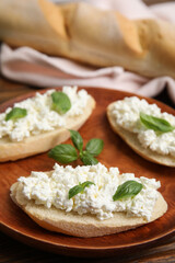 Bread with cottage cheese and basil on wooden plate, closeup