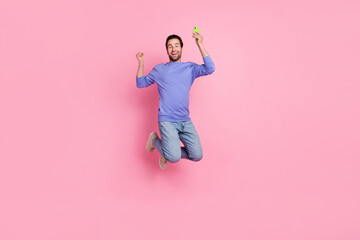 Full length photo of brunet cool millennial guy jump hold telephone wear blue pullover jeans sneakers isolated on pink background