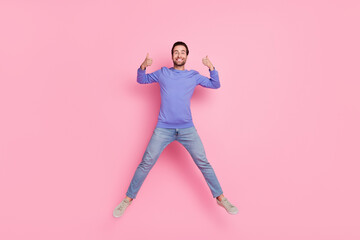 Full size photo of brunet impressed millennial guy jump show thumb up wear blue pullover jeans shoes isolated on pink background