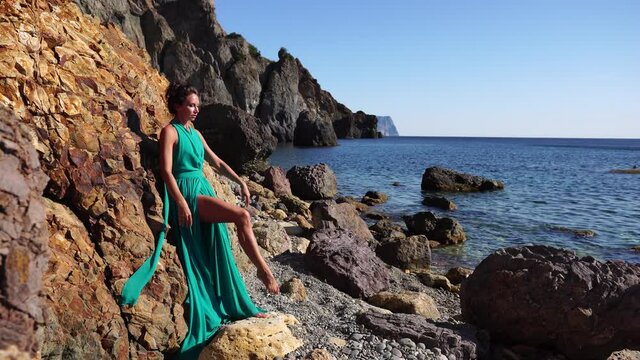Side view a Young beautiful sensual woman with black hair in a long mint dress posing on a beach with calm sea bokeh lights on sunny day. Girl on the nature on blue sky background. Fashion photo