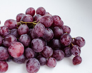 Purple grapes on a white background with drops on the fruits