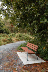 Brand new brown bench with metal frame and plastic parts installed on a concrete base by a small footpath in a park. Solid and practical design