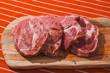 Four rib eye steaks on a wooden cutting board on a red and white apron. Premium top quality fresh meat. Butcher craft and food supply chain industry.