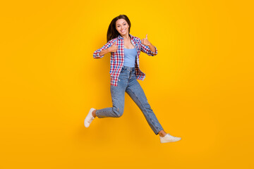 Fototapeta na wymiar Full length photo of promoter lady jump show thumbs up run fast wear plaid shirt isolated yellow color background