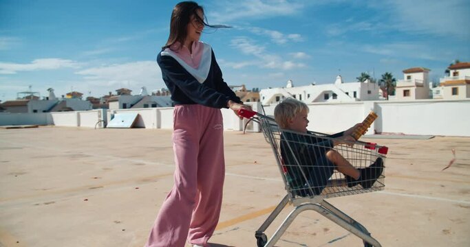 Happy family having fun on roof of supermarket with shopping cart and firecracker confetti explosion. Son and young mother spending time together on vacation shopping. Carefree childhood on sunny day