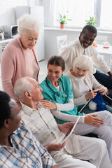 Nurse sitting near interracial patients with digital tablet and yarn in nursing home