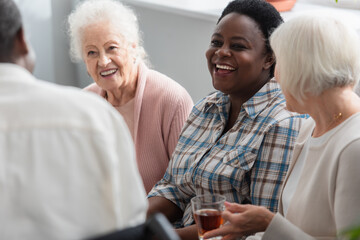 Cheerful interracial elderly people with tea talking in nursing home