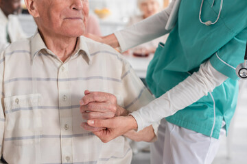Cropped view of nurse holding hand of senior patient in nursing home