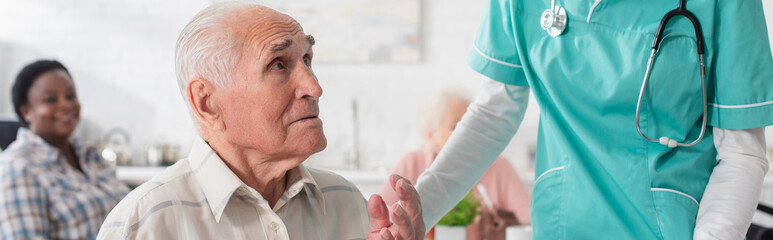 Senior man talking near nurse in nursing home, banner