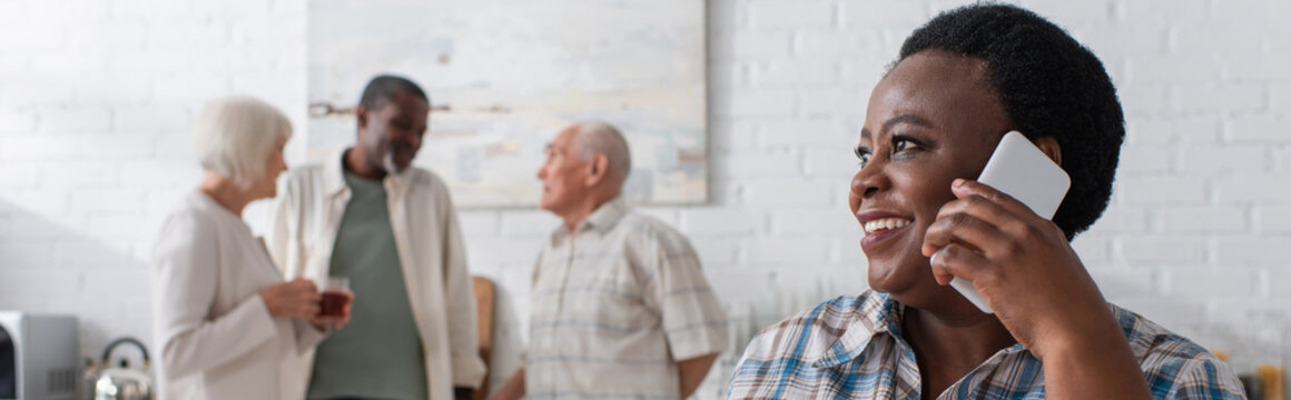 Cheerful African American Woman Talking On Smartphone Near Blurred Friends In Nursing Home, Banner