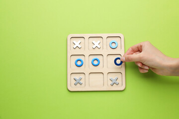 Woman playing tic tac toe game on light green background, top view
