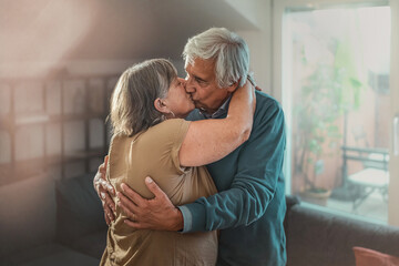 Senior couple tenderly hugging and kissing at home in the living room
