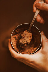 A woman holds a jar with crumbly natural cocoa powder in her hands and takes out a portion of cocoa with a silver teaspoon. Preparation of a pleasant drink in the morning.