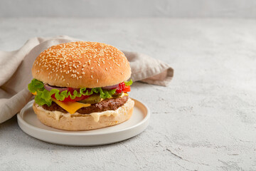 Classic traditional cheeseburger with beef, tomato, lettuce, pickles and onion on gray background