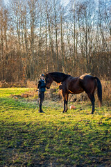 Happy girl looking after horse after riding - obrazy, fototapety, plakaty