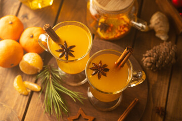 Two glass mugs with sea buckthorn tea. Hot yellow drink with cinnamon sticks and stars of star anise
