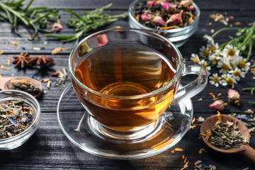 Composition with freshly brewed tea and different leaves on black wooden table, closeup
