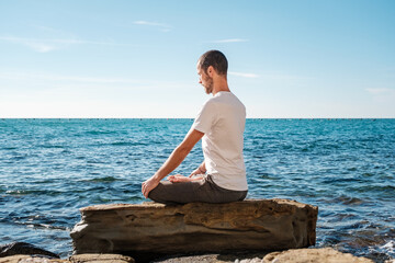 Attractive young man practicing yoga meditation and breath work outdoors by the sea
