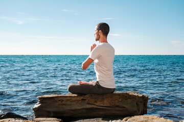 Attractive young man practicing yoga meditation and breath work outdoors by the sea
