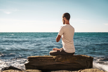 Naklejka premium Attractive young man practicing yoga meditation and breath work outdoors by the sea 
