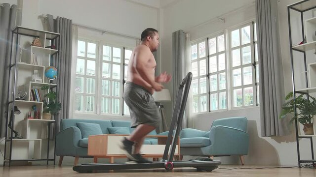 Asian Fat Man Wearing No T-Shirt And Running On A Treadmill At Home
