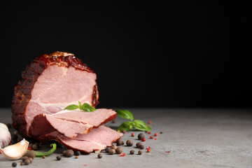 Delicious ham with spices, garlic and basil on grey table against black background, space for text