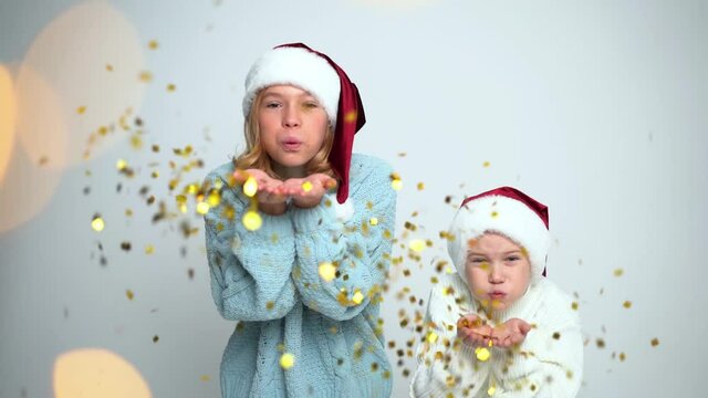 Happy Young girl and boy in Santa Claus caps blowing confetti. Concept Christmas