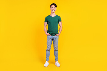 Fototapeta premium Full length photo of cheerful happy positive man hold hands pockets denim jeans isolated on yellow color background