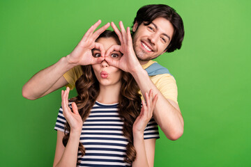 Photo of young crazy couple happy positive smile make fingers binoculars glasses isolated over green color background