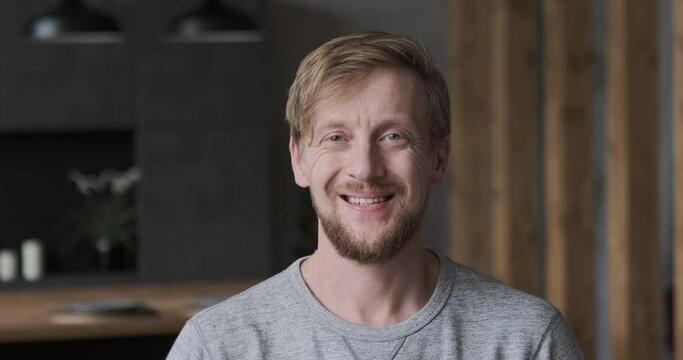 Closeup portrait of smiling European blonde guy posing at luxury apartment loft interior. Face of confident casual successful business male freelancer employee self employment boss or modern happy man
