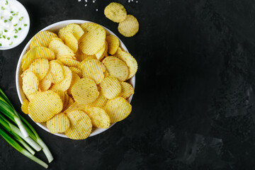 Obraz na płótnie Canvas Potato chips. Crispy potato chips and sour cream with onion in bowl on a dark stone concrete background