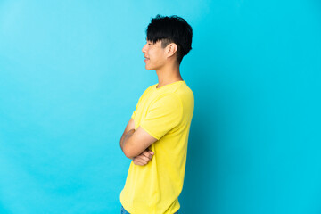 Young Chinese man isolated on blue background in lateral position