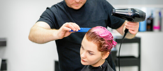 A hairdresser is drying the pink hair of the young woman in a beauty salon
