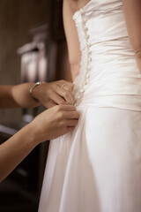 Obraz na płótnie Canvas Close up bride assistant hands prepare back of white brides wedding dress low angle view background