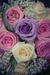 Close up top view golden wedding rings lay on beautiful purple white pink purple rose bridal bouquet background