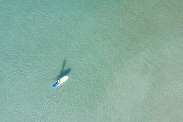 Aerial view of Asian man exercising sup board in turquoise tropical clear waters in summer day..
