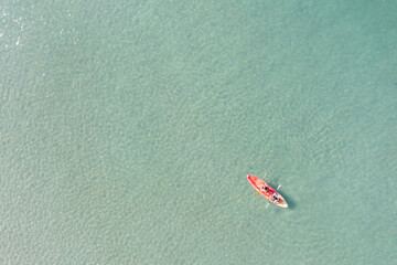 Aerial view of blue sea with couple and floating colorful kayak is going into sand beach, person...