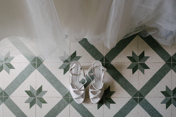 Top down view pair of white bridal high heel shoes on stylish floor isolated indoor by white wedding dress on display
