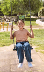 Happy kid girl having fun with chain swing on playground in a park