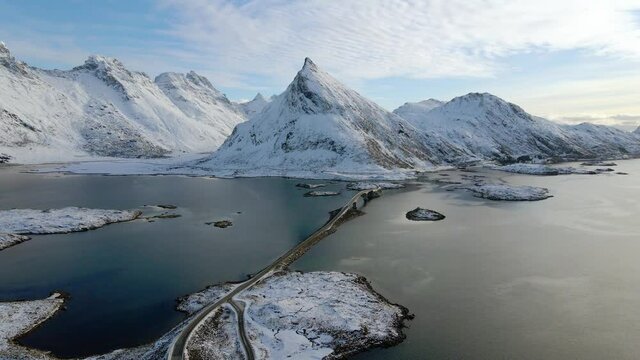 Aerial view over bridge and sea, snowy peaks in the background, in Norway - reverse, drone shot