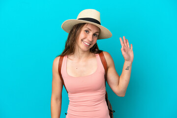 Fototapeta premium Young caucasian woman in summer holidays isolated on blue background saluting with hand with happy expression