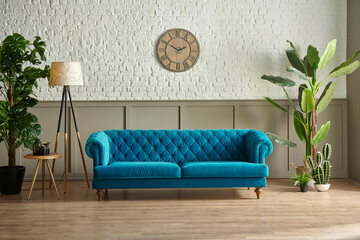 Blue quilted sofa in front of the brown classic grid and white brick wall, blanket vase of green...