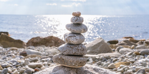 A pyramid of round stones (ladza) on a rocky beach against a blurred background of a sunny path on a restless sea surface
