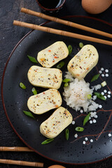 Closeup of sliced tamagoyaki or sweetened japanese egg roll on a black plate, vertical shot, top view