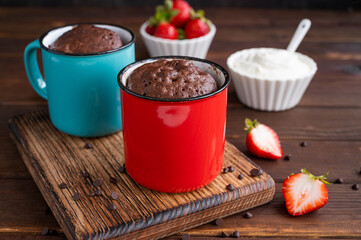 Chocolate mug cake with whipped cream and fresh berries on a dark wooden background. Cupcake cooked...
