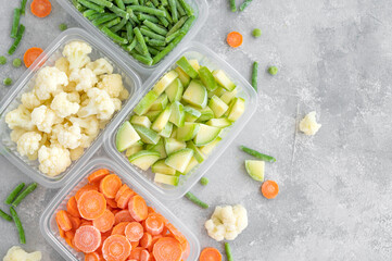 A variety of frozen vegetables in plastic containers on a gray concrete background. Healthy food. Copy space.