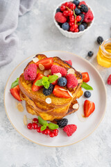 A stack of French toast on a plate with fresh berries, almond petals and honey on a gray concrete background. Delicious breakfast. Copy space.