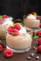 Chocolate mousse with whipped cream and fresh raspberries in a glass on a dark wooden background. Copy space.