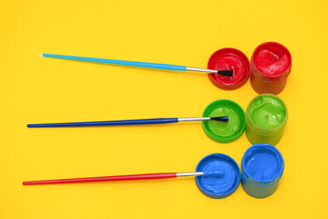 Three paintbrushes and gouaches of different colors: red, green, blue on yellow background